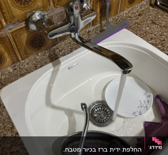 ברז מים זורמים בכיור עם כלים לניקוי